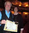 A couple holding a certificate and seat plaque
