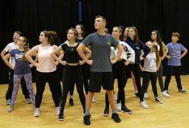 Children standing on a stage in a v formation, hands on hips, heads up.